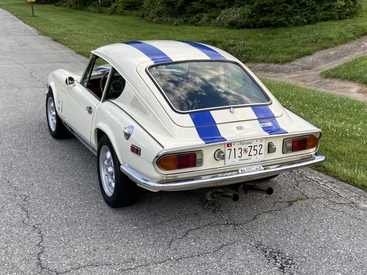 Restored 1973 Triumph GT6 rear view in white, with blue strips and dual exhaust